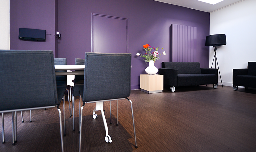 Een ruimte met stoelen en banken en een paarse muur